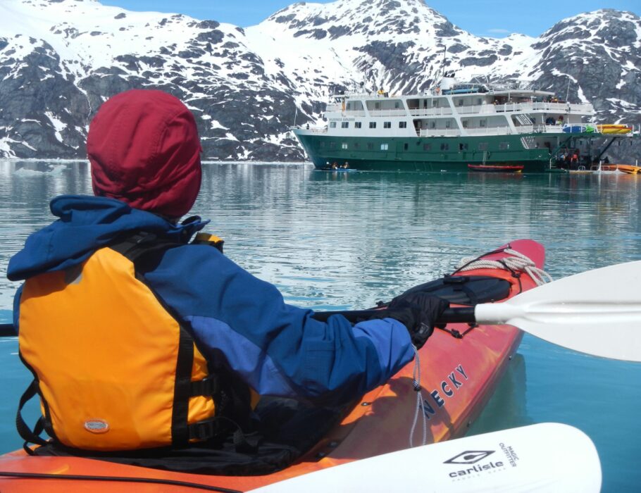 sea kayaker looking at Alaska glacier cruise ship and snow covered mountains