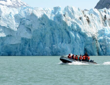 skiff below towering glacier in Glacier Bay