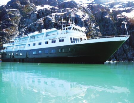 Wilderness Explorer cruise ship floating in bay with snow on mountains behind