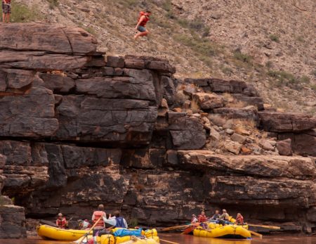 rafters watch someone jumping from a rock into the Colorado River