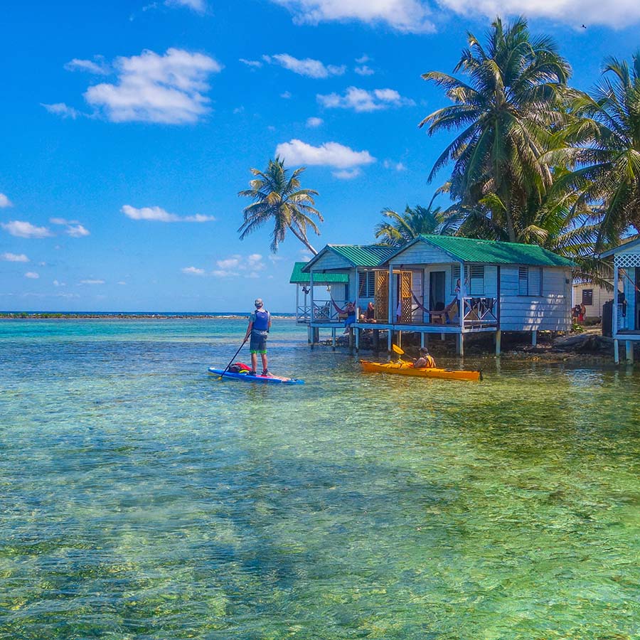 stand up paddle boarder in front of waterside accommodations in Caribbean
